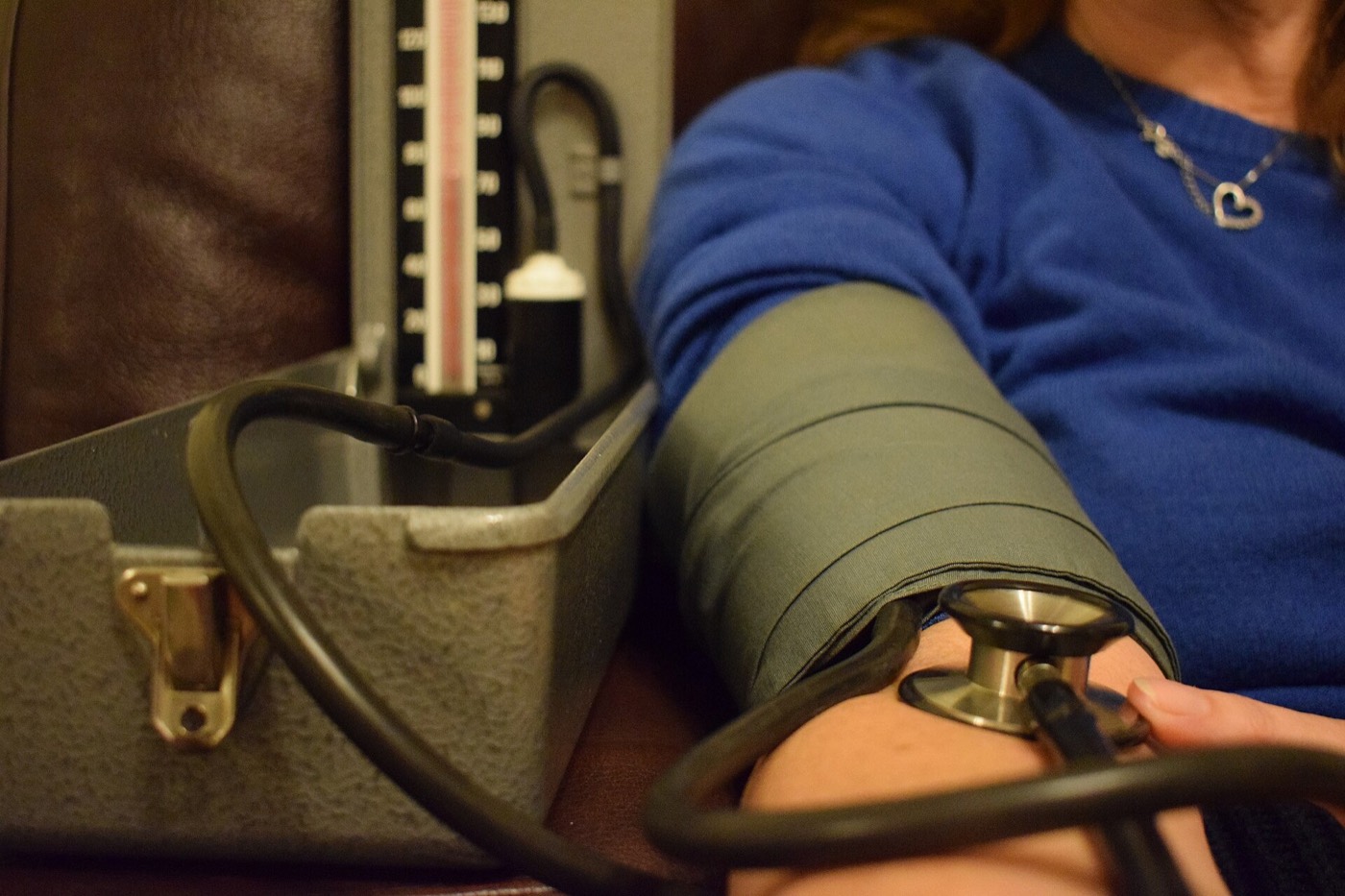 An upper-arm blood pressure cuff on a person's arm beside a manual gauge, with a stethoscope held at the elbow