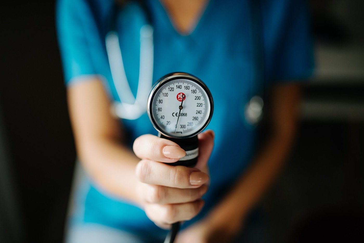 A clinician in scrubs holds up the round gauge of a blood pressure cuff